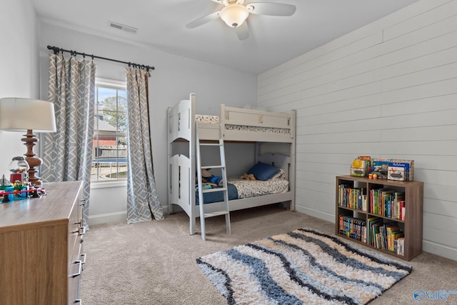 carpeted bedroom with wooden walls, visible vents, a ceiling fan, and baseboards