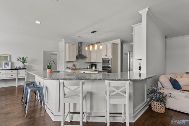 kitchen with a sink, stainless steel microwave, dark wood-style flooring, wall chimney range hood, and ornamental molding