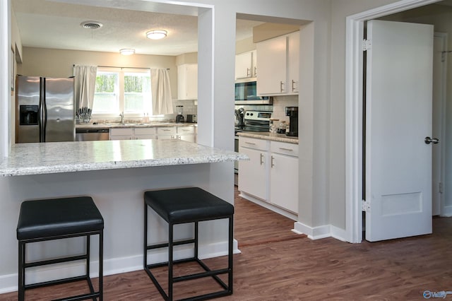 kitchen featuring a peninsula, visible vents, white cabinets, appliances with stainless steel finishes, and dark wood-style floors