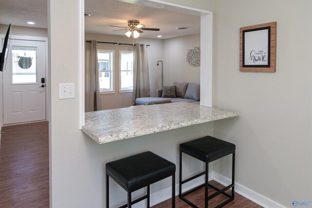 kitchen with dark wood-style floors, a kitchen breakfast bar, baseboards, and recessed lighting