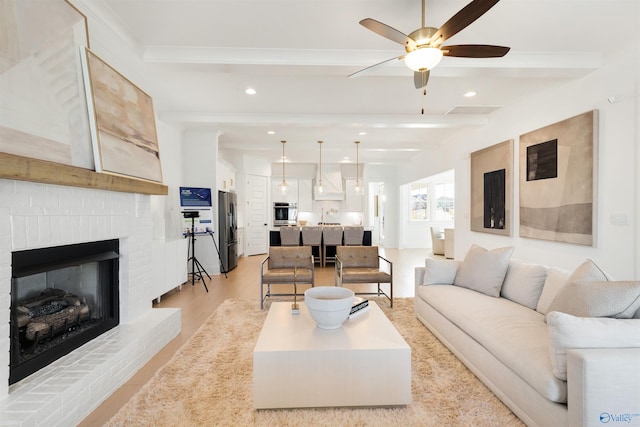 living room with beam ceiling, a fireplace, light hardwood / wood-style floors, and ceiling fan