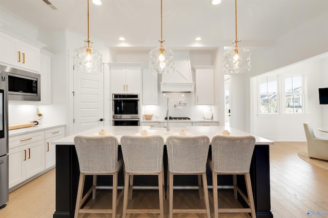 kitchen with stainless steel appliances, white cabinetry, a center island with sink, and decorative light fixtures