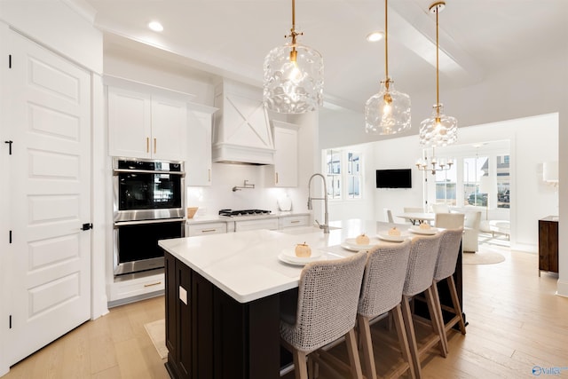 kitchen featuring pendant lighting, sink, double oven, an island with sink, and white cabinets