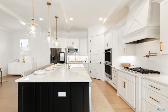 kitchen featuring appliances with stainless steel finishes, a kitchen island with sink, white cabinetry, decorative light fixtures, and custom exhaust hood