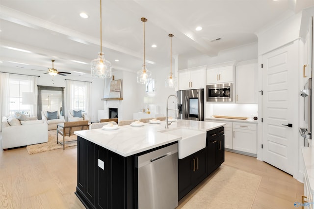 kitchen with appliances with stainless steel finishes, decorative light fixtures, white cabinetry, sink, and a center island with sink