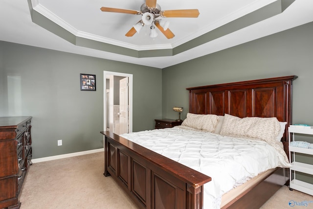 carpeted bedroom with ceiling fan, a raised ceiling, ornamental molding, and ensuite bath