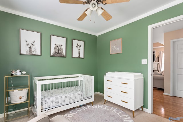 bedroom with carpet flooring, a nursery area, crown molding, and ceiling fan