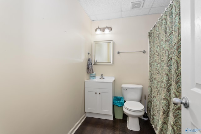 bathroom with wood-type flooring, vanity, toilet, and a drop ceiling