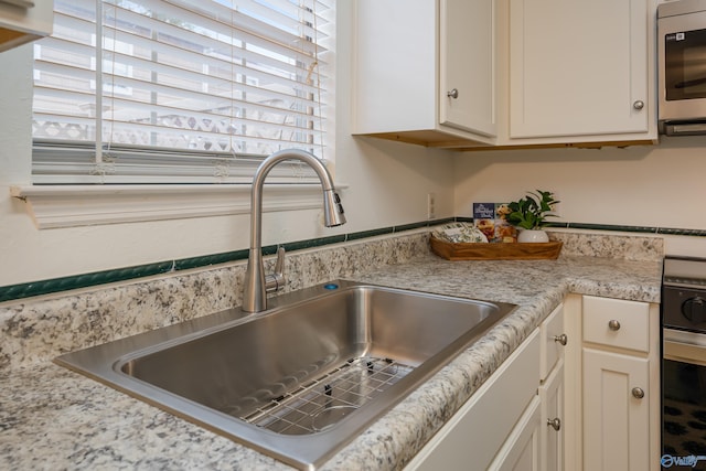 room details featuring white cabinets, sink, and light stone counters