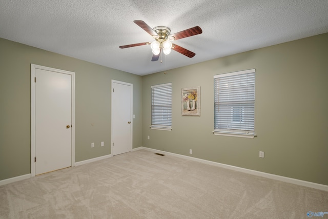 unfurnished bedroom with two closets, a textured ceiling, light colored carpet, and ceiling fan