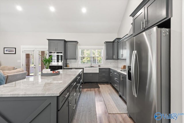 kitchen with gray cabinets, backsplash, appliances with stainless steel finishes, dark hardwood / wood-style flooring, and light stone countertops