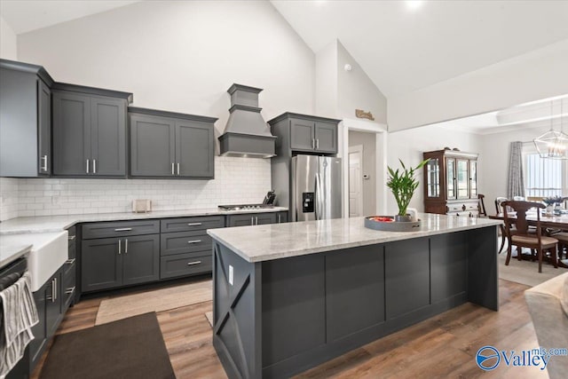 kitchen with appliances with stainless steel finishes, custom range hood, high vaulted ceiling, hardwood / wood-style flooring, and a chandelier