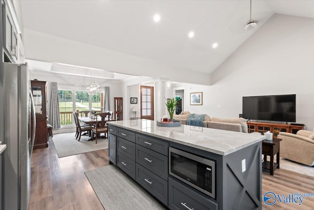 kitchen with wood-type flooring, hanging light fixtures, a kitchen island, stainless steel appliances, and ornate columns