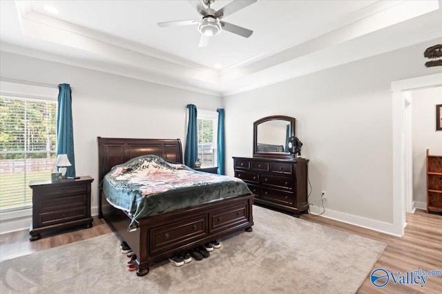 bedroom featuring ceiling fan, a tray ceiling, crown molding, and light hardwood / wood-style floors