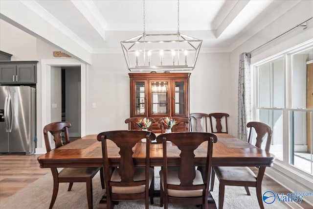 dining space with wood-type flooring, an inviting chandelier, a tray ceiling, and crown molding