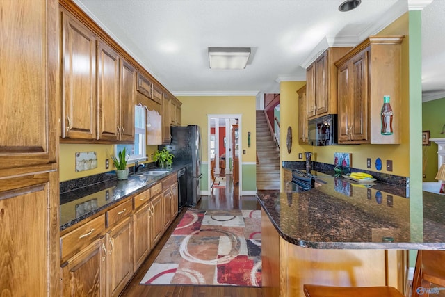 kitchen with a sink, black appliances, brown cabinetry, and ornamental molding