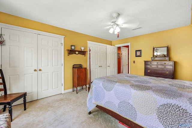 bedroom with visible vents, ceiling fan, a textured ceiling, light carpet, and two closets