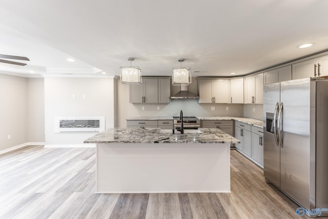 kitchen with light wood finished floors, wall chimney range hood, light stone counters, gray cabinets, and stainless steel appliances