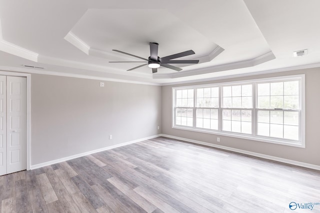 empty room featuring visible vents, a ceiling fan, a tray ceiling, wood finished floors, and crown molding