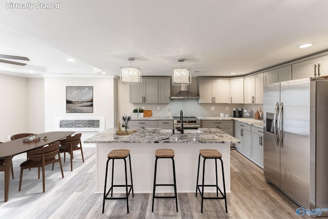 kitchen with wall chimney range hood, gray cabinets, light wood-style flooring, stainless steel appliances, and a sink