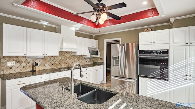 kitchen featuring white cabinetry, sink, black appliances, a raised ceiling, and custom range hood