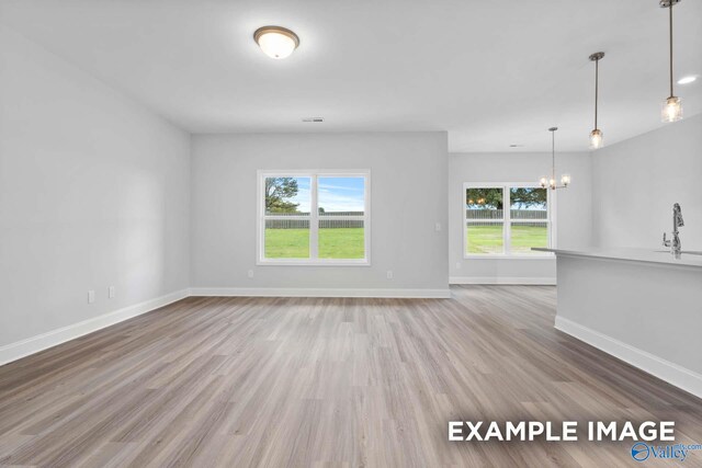 unfurnished living room with a chandelier, a wealth of natural light, sink, and wood-type flooring