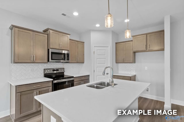 kitchen with wood-type flooring, appliances with stainless steel finishes, an island with sink, and sink