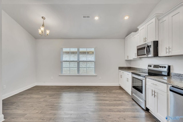 kitchen featuring pendant lighting, dark stone countertops, hardwood / wood-style floors, stainless steel appliances, and white cabinets