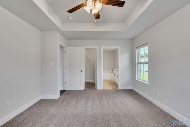 unfurnished bedroom featuring a walk in closet, light colored carpet, ceiling fan, a raised ceiling, and ensuite bath