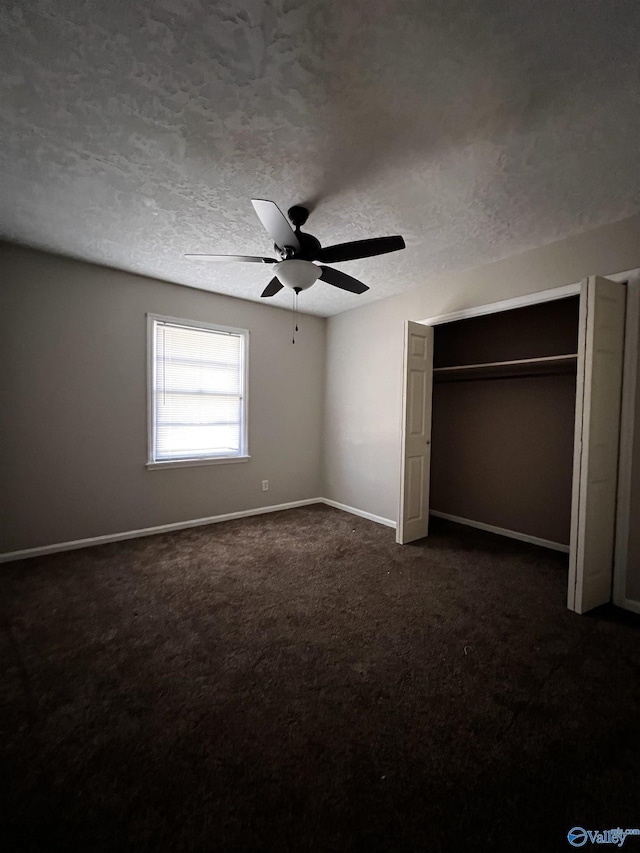 unfurnished bedroom featuring baseboards, ceiling fan, dark carpet, a closet, and a textured ceiling