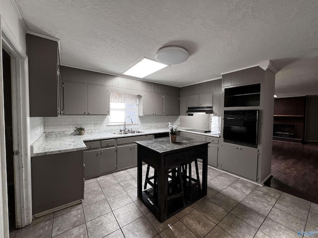 kitchen featuring tasteful backsplash, gray cabinetry, under cabinet range hood, black appliances, and a sink