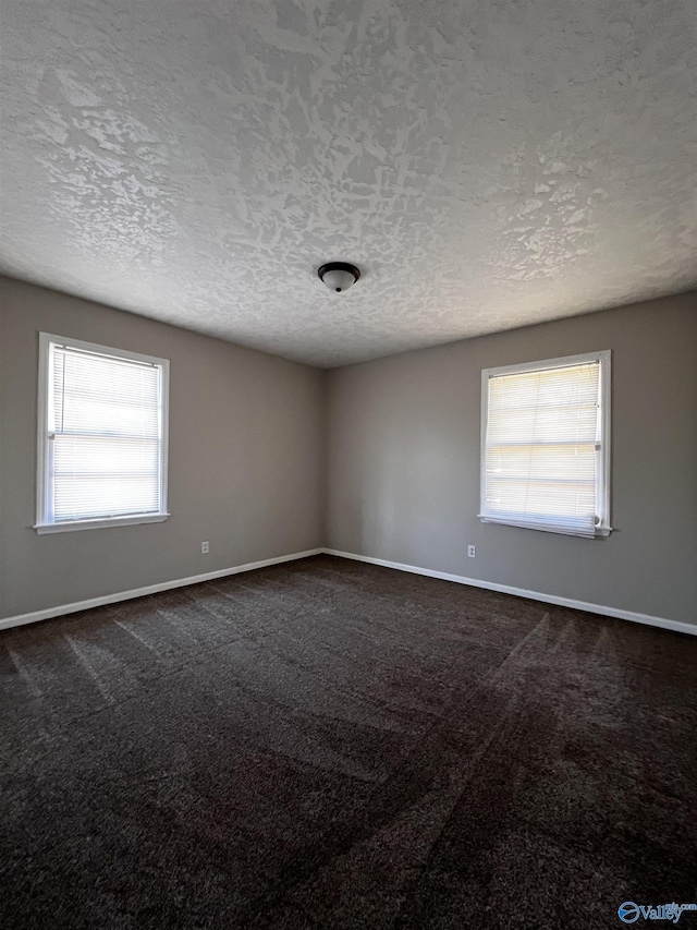 empty room with baseboards, dark carpet, and a textured ceiling