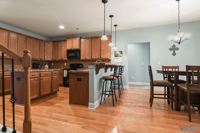 kitchen featuring brown cabinetry, decorative backsplash, a kitchen breakfast bar, and black appliances
