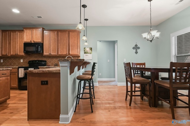 kitchen featuring tasteful backsplash, dark countertops, a breakfast bar area, light wood-type flooring, and black appliances