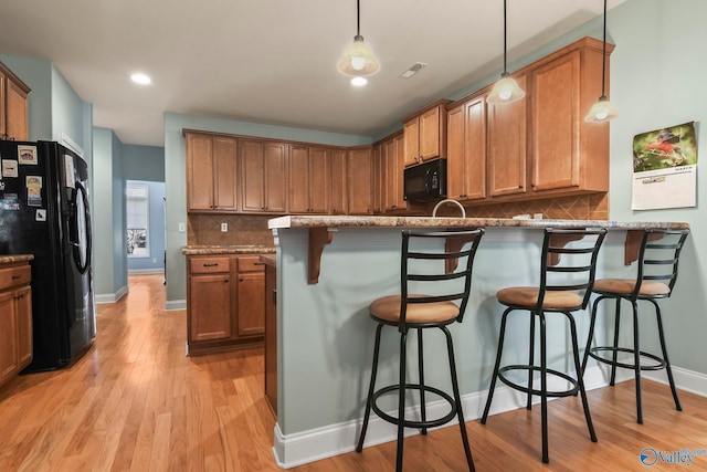 kitchen with a kitchen bar, black appliances, light wood-style flooring, a peninsula, and decorative backsplash