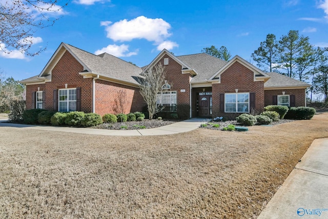 view of front facade with a front yard, brick siding, and a shingled roof