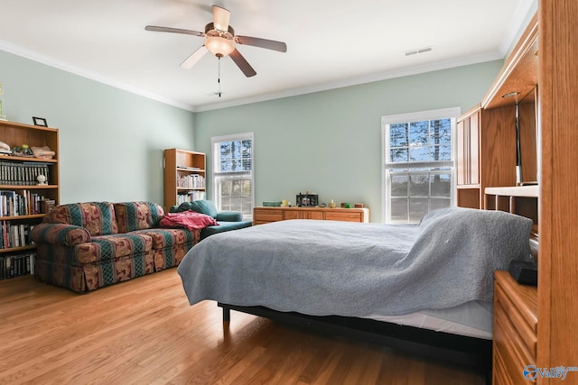 bedroom with a ceiling fan, crown molding, wood finished floors, and visible vents