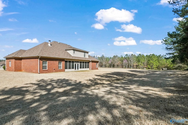 rear view of house with a sunroom, brick siding, and a shingled roof