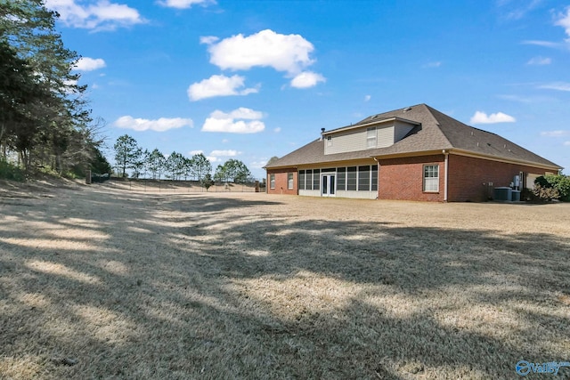 exterior space featuring central air condition unit, brick siding, roof with shingles, and a yard