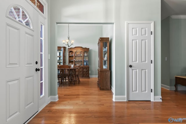 entryway featuring an inviting chandelier, a high ceiling, light wood-style floors, and baseboards