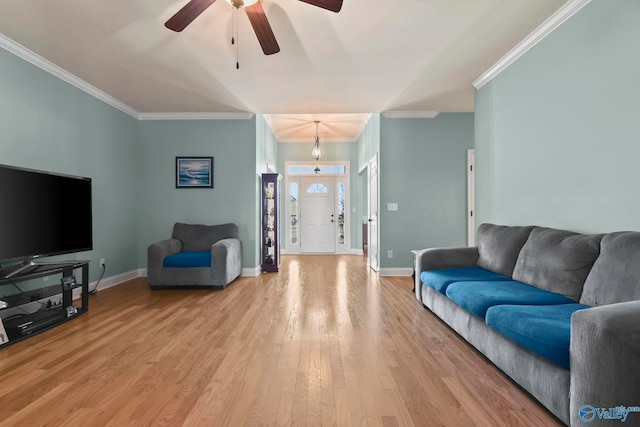 living area with baseboards, light wood-style floors, ornamental molding, and a ceiling fan