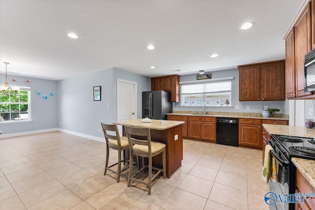 kitchen featuring a center island, a sink, light tile patterned floors, black appliances, and a breakfast bar