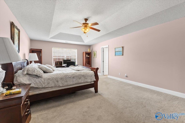 bedroom featuring baseboards, light colored carpet, a textured ceiling, a raised ceiling, and a ceiling fan