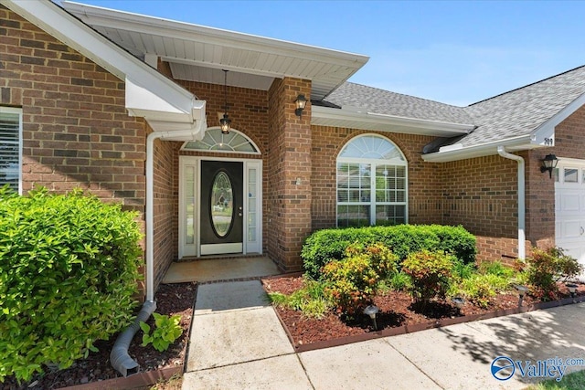 view of exterior entry featuring brick siding, a garage, and roof with shingles