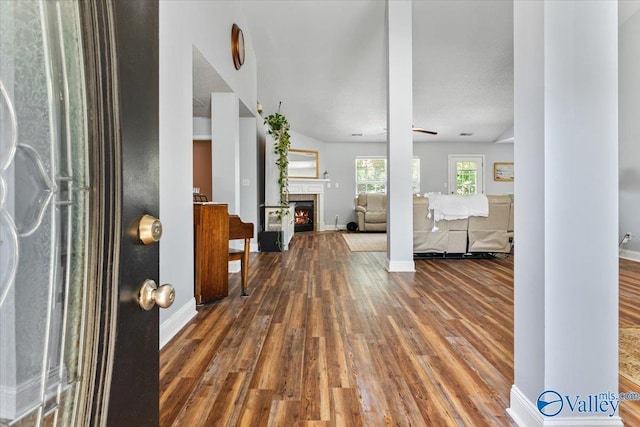 foyer entrance featuring baseboards, decorative columns, wood finished floors, and a lit fireplace