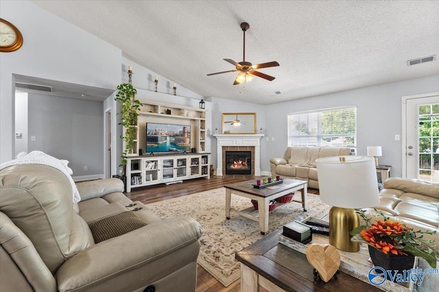 living room featuring a textured ceiling, a ceiling fan, wood finished floors, vaulted ceiling, and visible vents