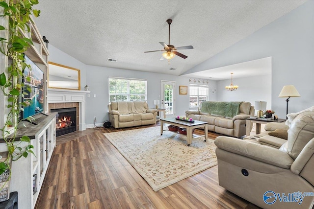 living room with a fireplace, a textured ceiling, dark wood finished floors, ceiling fan with notable chandelier, and lofted ceiling