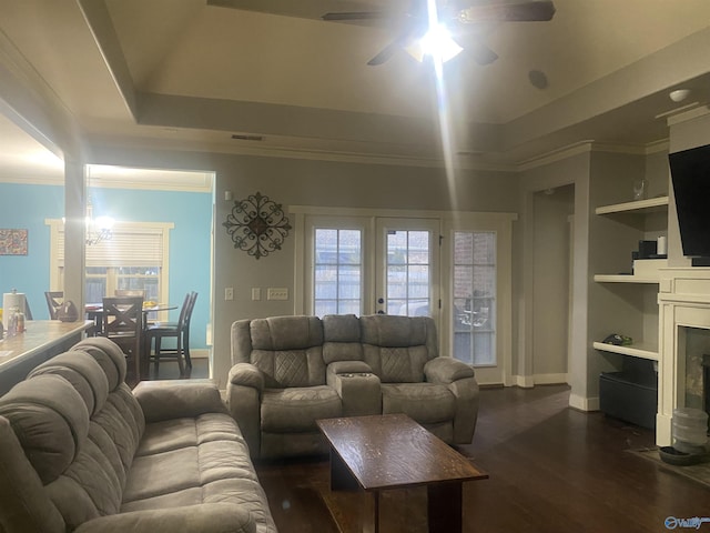 living area featuring a tray ceiling, dark wood-type flooring, ornamental molding, and a ceiling fan