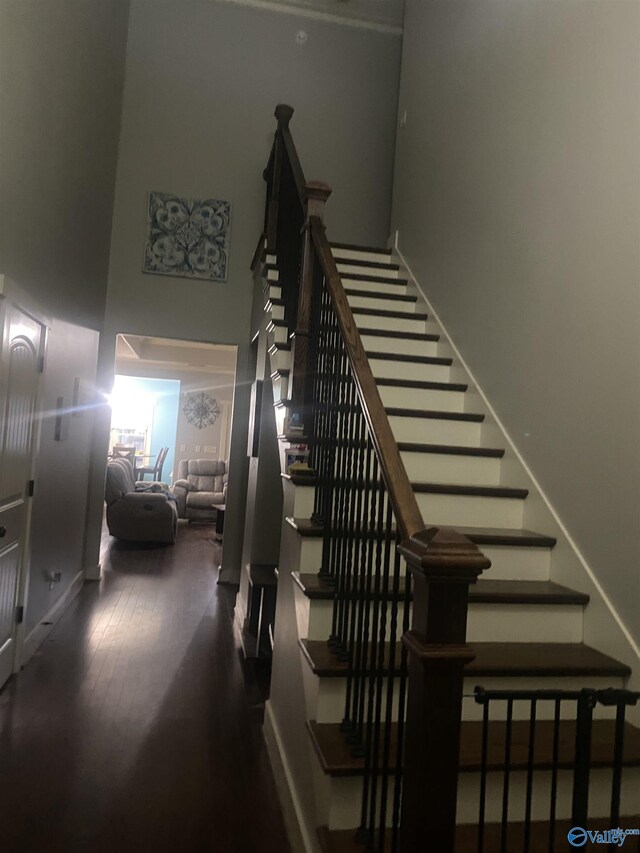 stairway featuring a high ceiling, wood finished floors, and baseboards