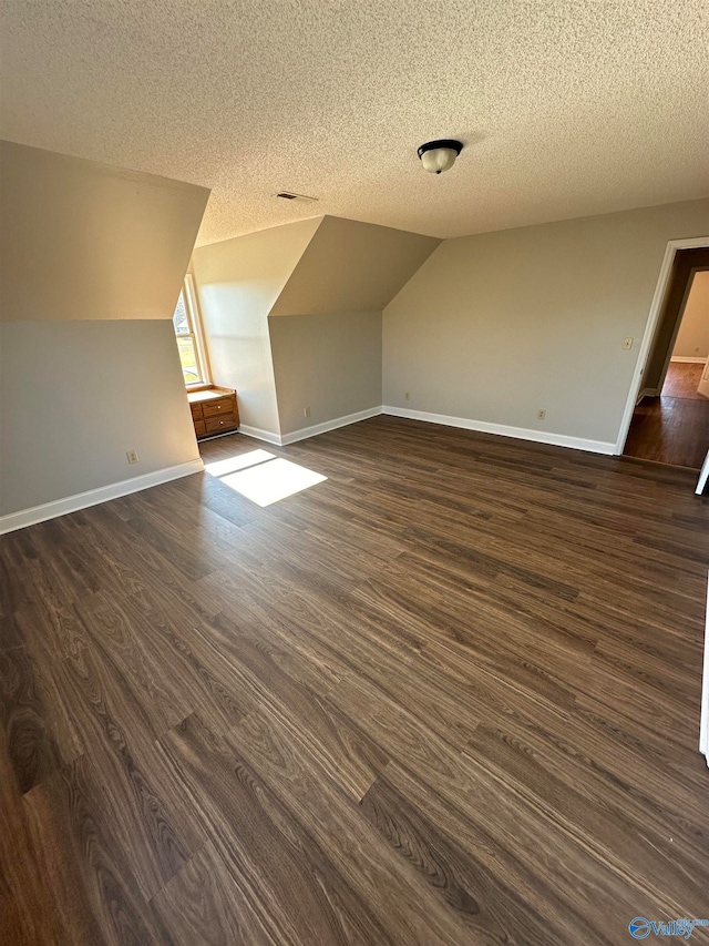 additional living space featuring dark hardwood / wood-style flooring, a textured ceiling, and vaulted ceiling